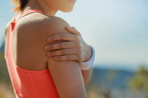 woman outside in orange tank top clenching frozen shoulder