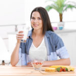 woman with milk and healthy breakfast in kitchen